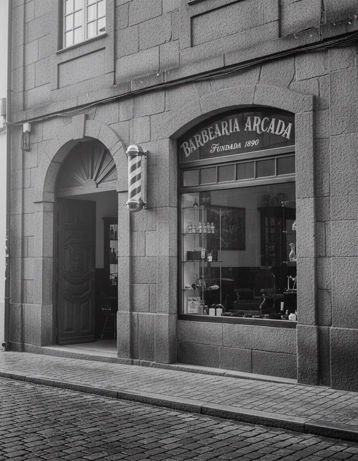 Fachada de granito da Barbearia Arcada numa rua de pedra de Braga, com letras pintadas na montra e poste de barbeiro junto à porta